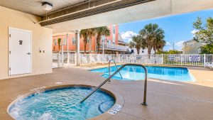 cherry-grove-207-hot-tub | Swack Vacations Outdoor pool area at a sunny apartment complex with palm trees, white fencing, and lounge chairs nearby (informational).