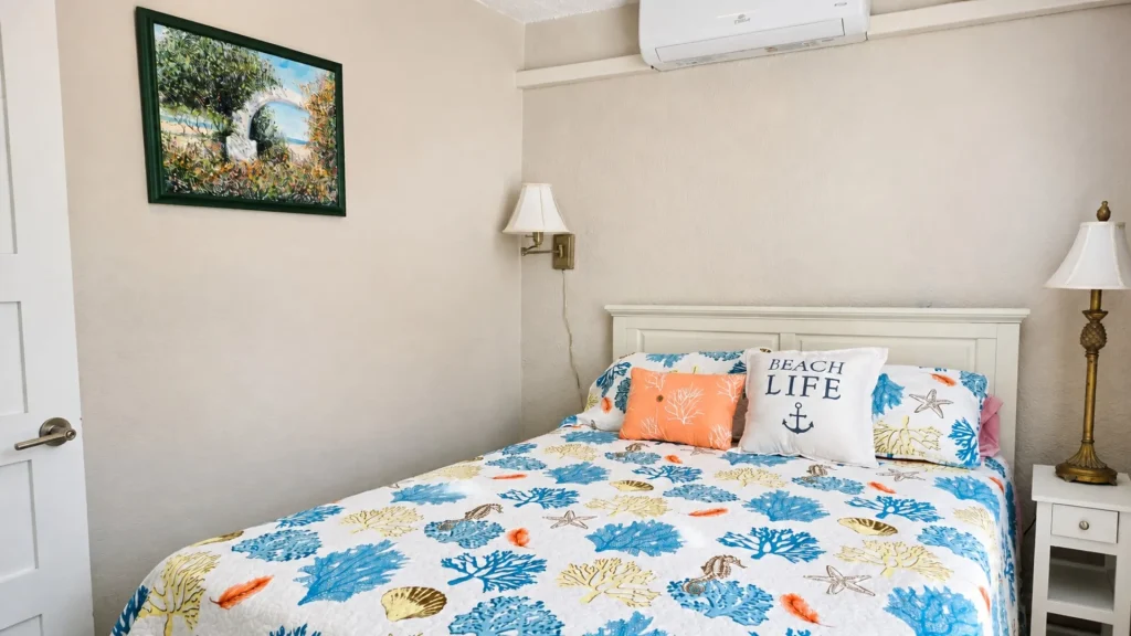Cozy beach-themed bedroom with a sea-shell patterned quilt and blue-yellow pillows on a white bed.