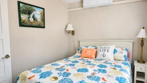 Cozy beach-themed bedroom with a sea-shell patterned quilt and blue-yellow pillows on a white bed.