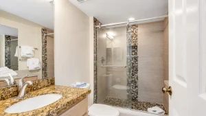 Modern bathroom with granite countertop, undermount sink, mirror, and glass shower with pebble mosaic columns.
