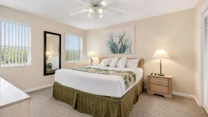 Hotel bedroom with a king bed, two nightstands, tropical bedding, and a ceiling fan with lights.”](Oops)