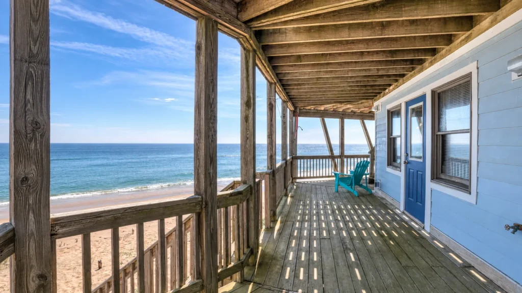 Beachfront wooden balcony with a blue door, turquoise chair, and expansive ocean view.
