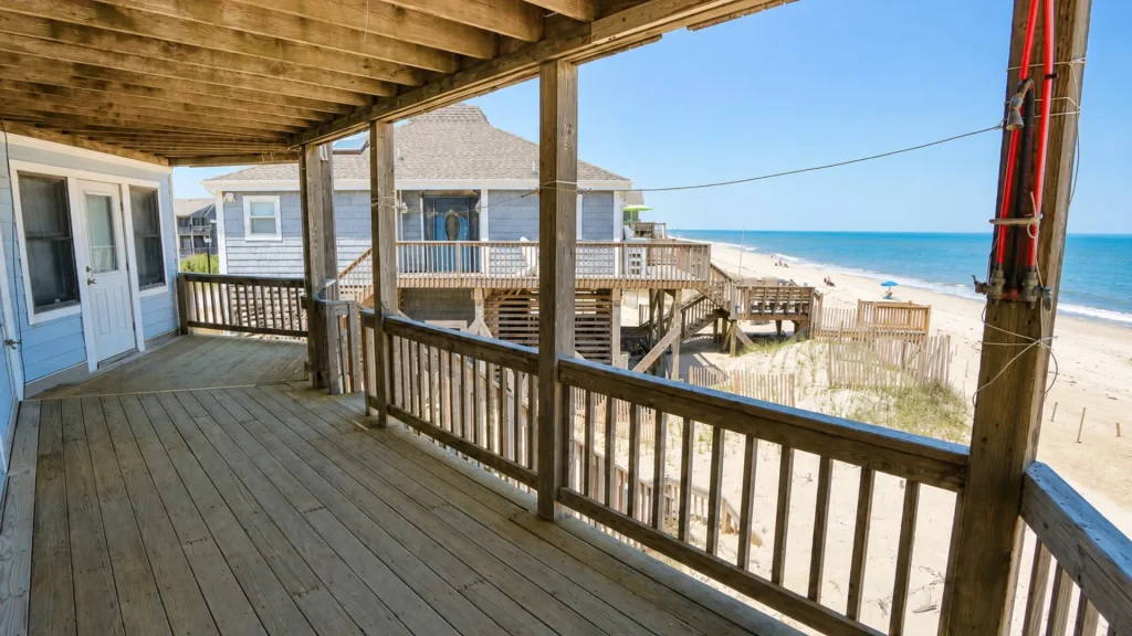 View from a wooden beach house deck overlooking the sandy shore and sea.