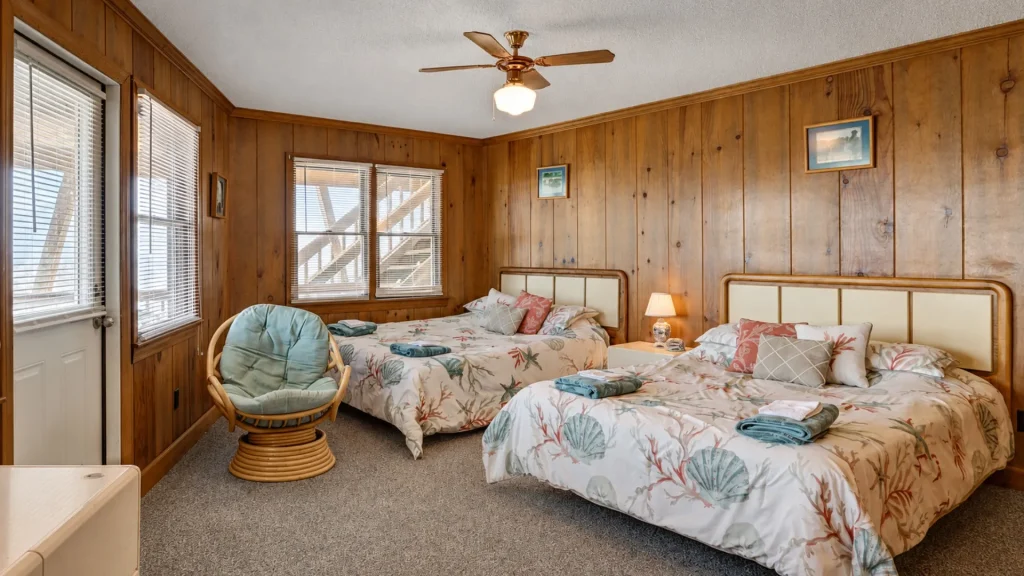 Twin bedroom with wood-paneled walls, two beds with seashell-themed bedding and a small nightstand lamp.