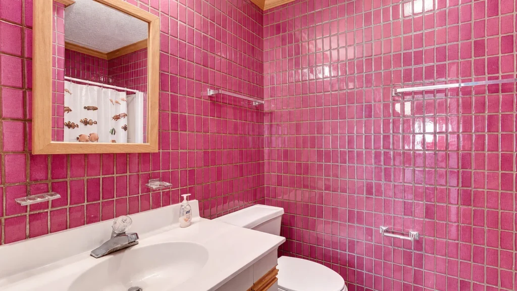 Pink tiled bathroom with a white sink, wooden-framed mirror, and chrome towel racks, in a retro style.