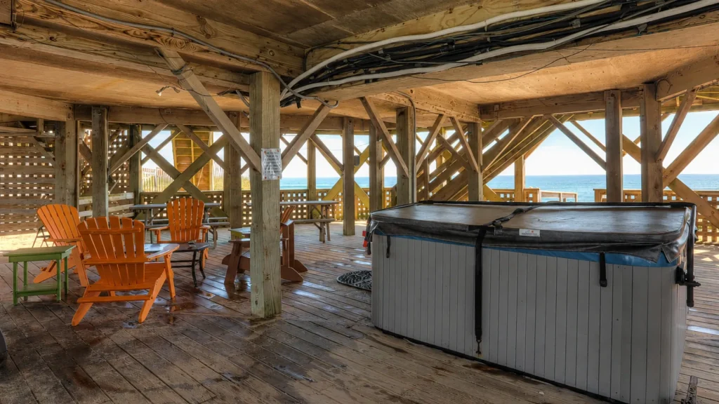 Wooden beach pavilion with orange Adirondack chairs, a hot tub, and an ocean view beyond the railing.