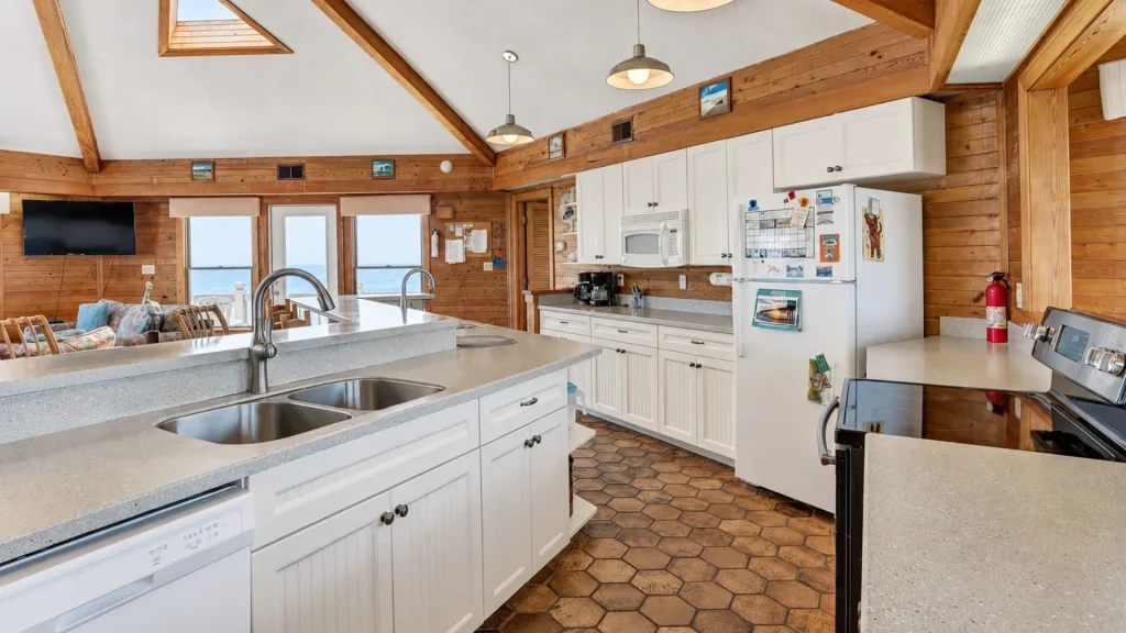 Bright cabin kitchen with white cabinets, island sink, and ocean view through the windows nearby.