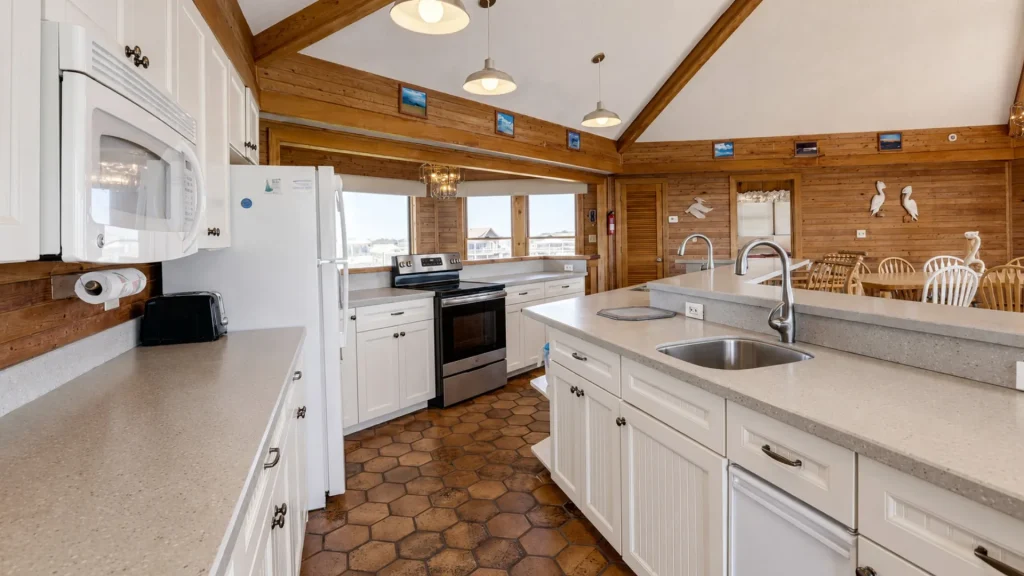 Open-concept kitchen with white cabinets, island, and stainless appliances in a wood-paneled cabin and a dining area beyond.