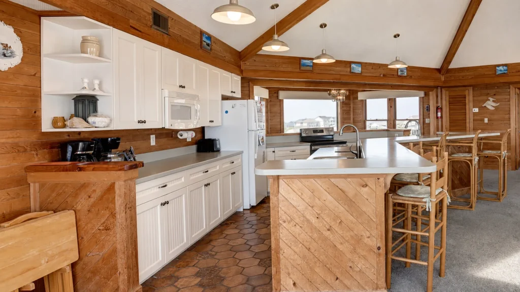 Rustic cabin kitchen with white cabinets, wooden walls and beams, and a central island with bar stools.