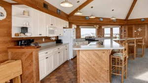 pompous-pelican-kitchen-3 | Swack Vacations Rustic cabin kitchen with white cabinets, wooden walls and beams, and a central island with bar stools.