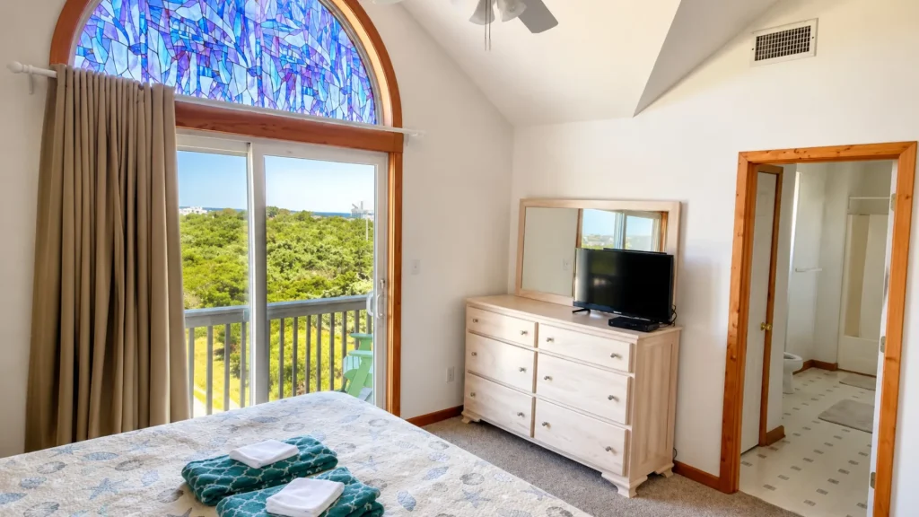 Bedroom with a sliding balcony door under a colorful arched stained-glass window; view of trees and blue sky outside