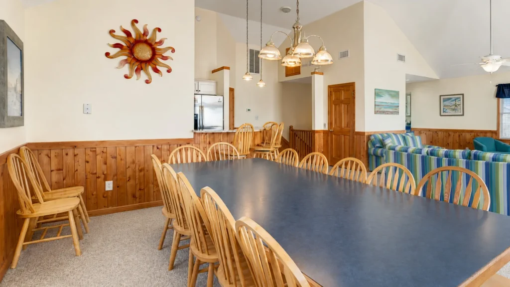 Large dining room with a long blue table, wooden chairs, and wood-paneled walls, accented by a sun sculpture on the wall.