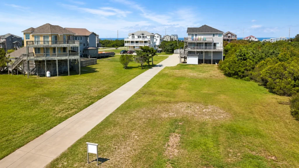 Aerial view of a coastal neighborhood with elevated houses on stilts lining a central concrete walkway toward the sea.