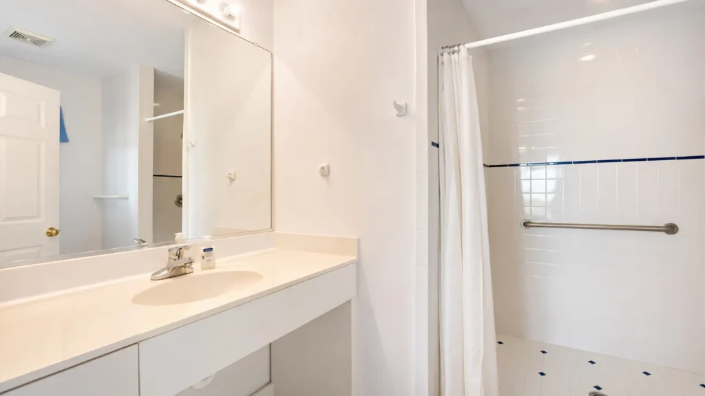 White bathroom with a vanity sink, large mirror, and a shower curtain at the right edge.