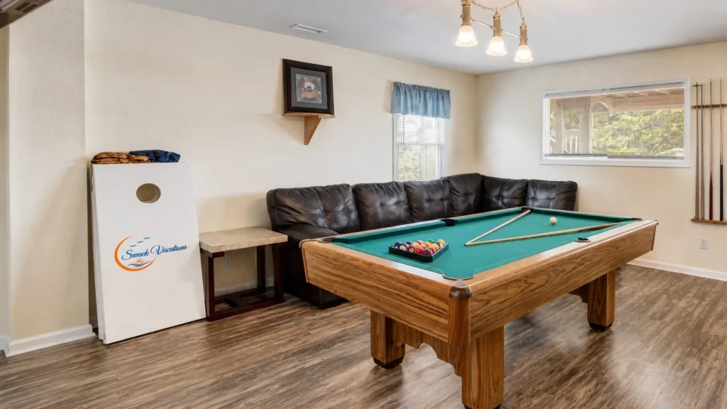 Pool table with green felt and a rack of billiard balls, backed by a black leather sectional in a cozy game room