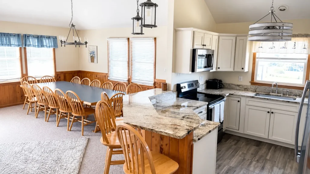 Open-concept kitchen and dining area with a long wooden table and many chairs, blue window valances, and granite countertops