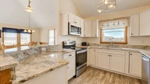 Bright kitchen with granite countertops, white cabinets, stainless steel stove and microwave, and a window view.