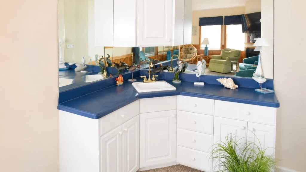 Blue bathroom vanity with white cabinets and brass faucet, adorned with sea figurines and shells on a blue countertop mirror reflecting a living room.
