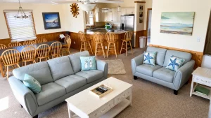 Bright open living area with light blue sofas and coastal pillows, a white coffee table, and a matching side table in front of carpeted floors.