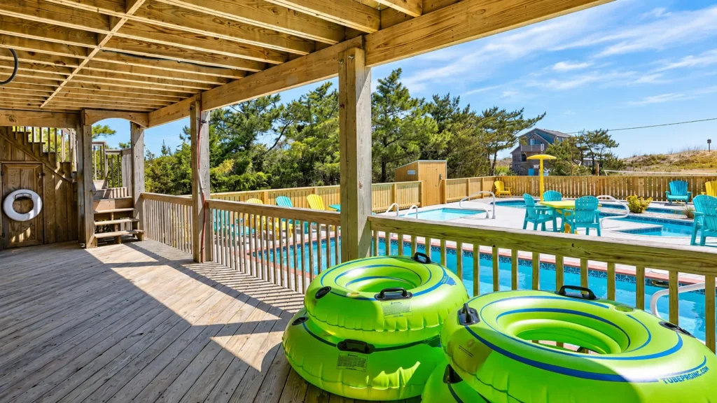 Wooden deck under a structure overlooks a pool with bright lime-green inflatable inner tubes in the foreground and colorful chairs around the water.