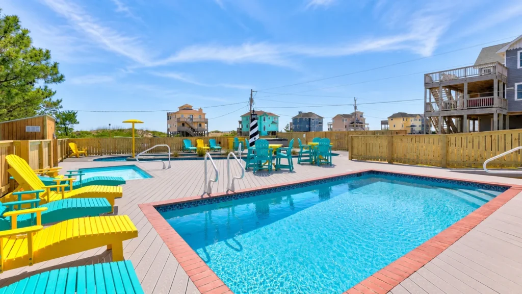 Colorful poolside scene with turquoise and yellow chairs around a bright blue swimming pool on a wooden deck, daytime sky above.