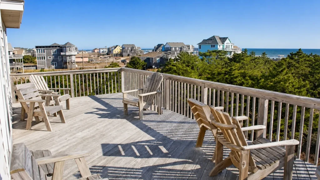 Wooden deck with Adirondack chairs overlooking a coastal neighborhood and the sea on a sunny day.