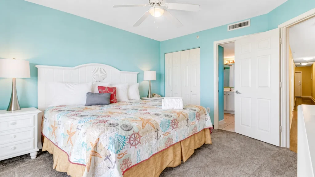 Bright coastal hotel bedroom with turquoise walls, white headboard, and seashell-themed quilt.
