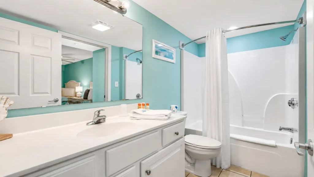Bright bathroom with teal walls, white vanity, large mirror, and a curved shower rod over a white tub/shower combination with a white curtain.