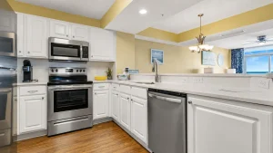 Bright modern kitchen with white cabinets and stainless steel appliances, yellow walls, and an ocean-view window.