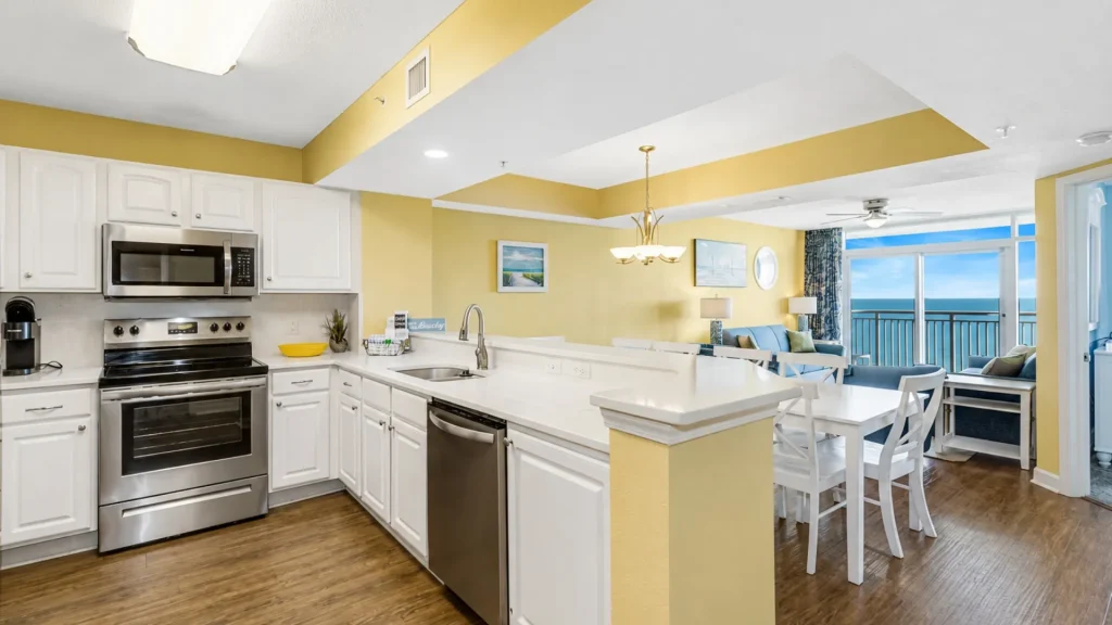 Open-concept kitchen with white cabinets, stainless steel appliances, and a yellow accent wall leading to a living area with an ocean view.