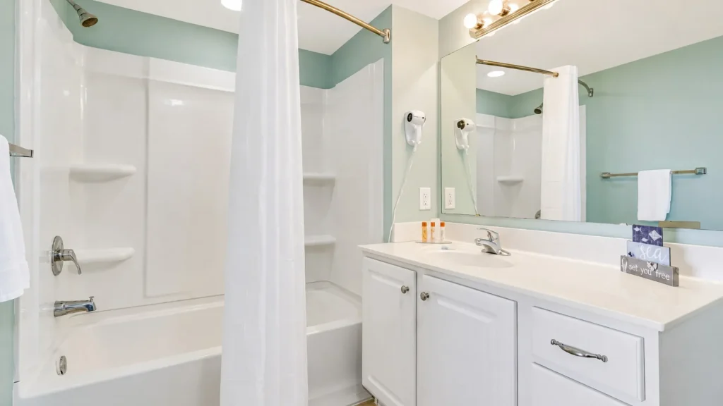 Bright bathroom with a white tub/shower, shower curtain, mint walls, and a white vanity with a large mirror to the right.