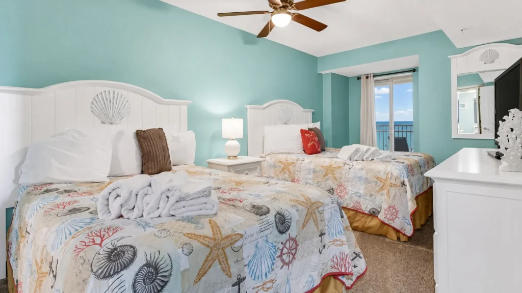 Twin bedroom with turquoise walls, white sea-shell headboards, and starfish quilts facing a balcony ocean view