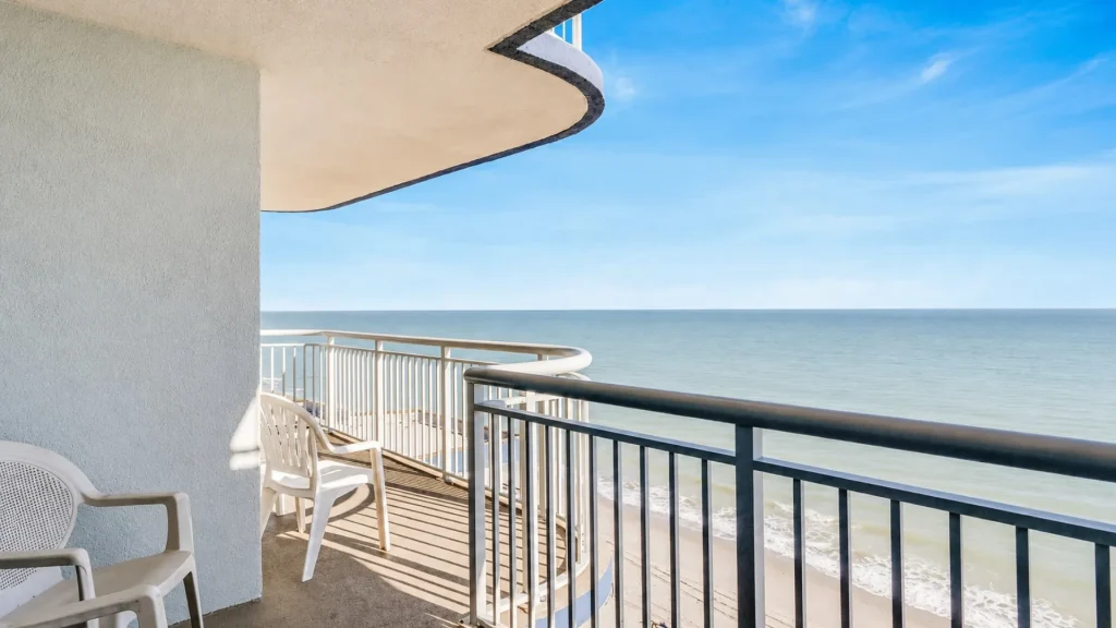 Balcony seating with white plastic chairs facing a calm ocean under a clear blue sky.