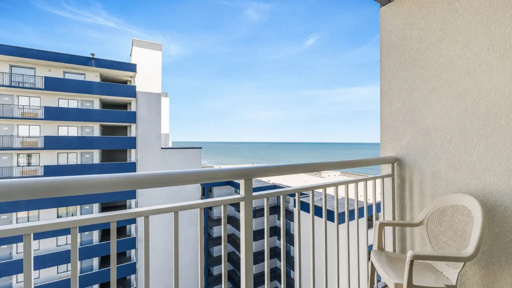 Balcony with two beige chairs overlooking the blue ocean and a white-blue apartment building.