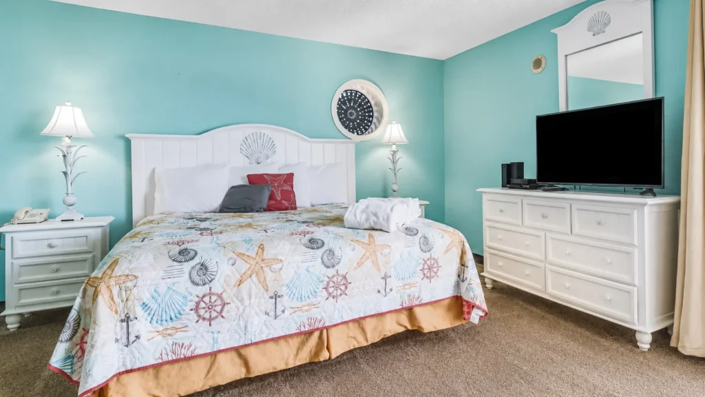 Beach-themed hotel room with white furniture, turquoise walls, and a shell-pattern quilt on the bed.