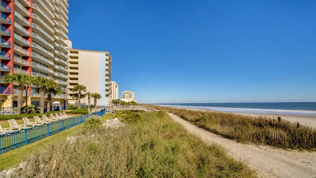 Beachfront hotel with colorful balconies, palm trees, and lounge chairs by a pool along the sandy shore.