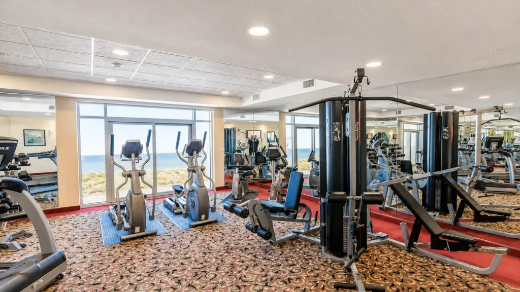 Well-equipped hotel gym with cardio machines facing large windows overlooking the ocean outside.]