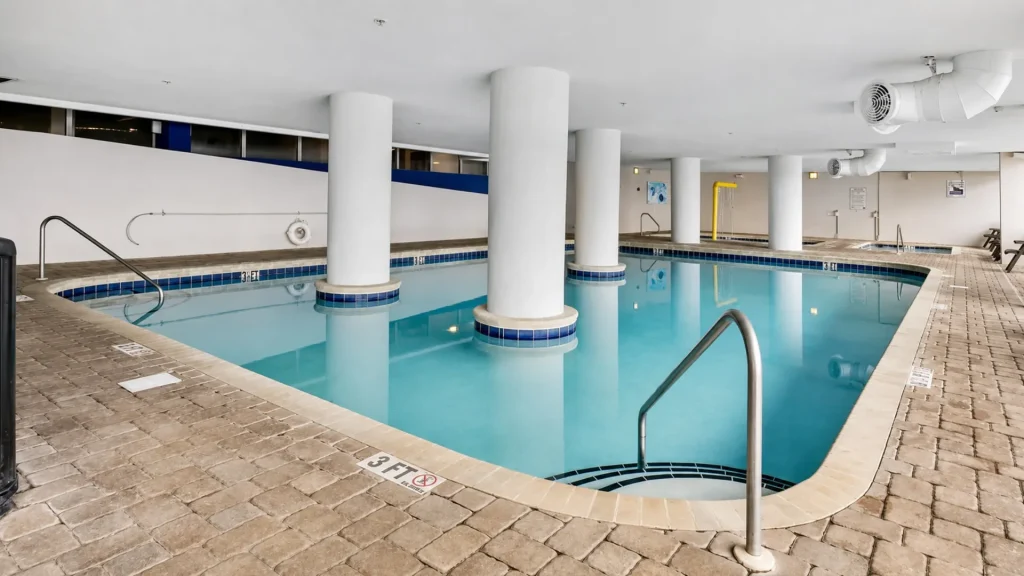 Indoor swimming pool with turquoise water, white columns, and a beige brick deck.