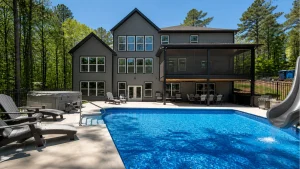 Modern gray, two-story house with large windows and a screened-in patio overlooking a blue pool area. corporate-adjacent: trees in the background and outdoor seating nearby.