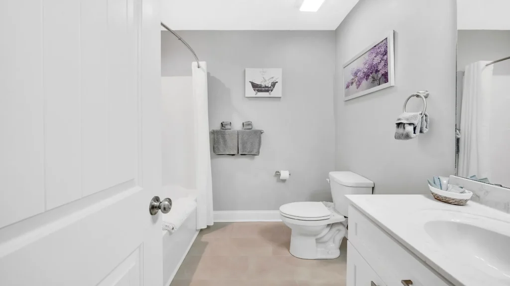 Modern gray bathroom with white tub, shower curtain, toilet, and vanity opposite.