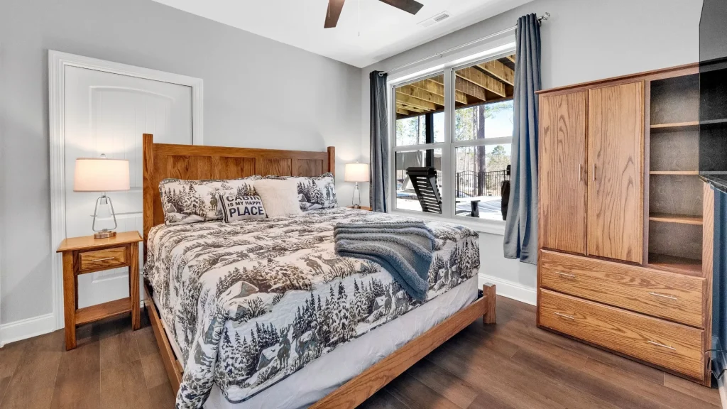 Cozy bedroom with a wooden bed, matching nightstands, and a large window with blue curtains letting in daylight.