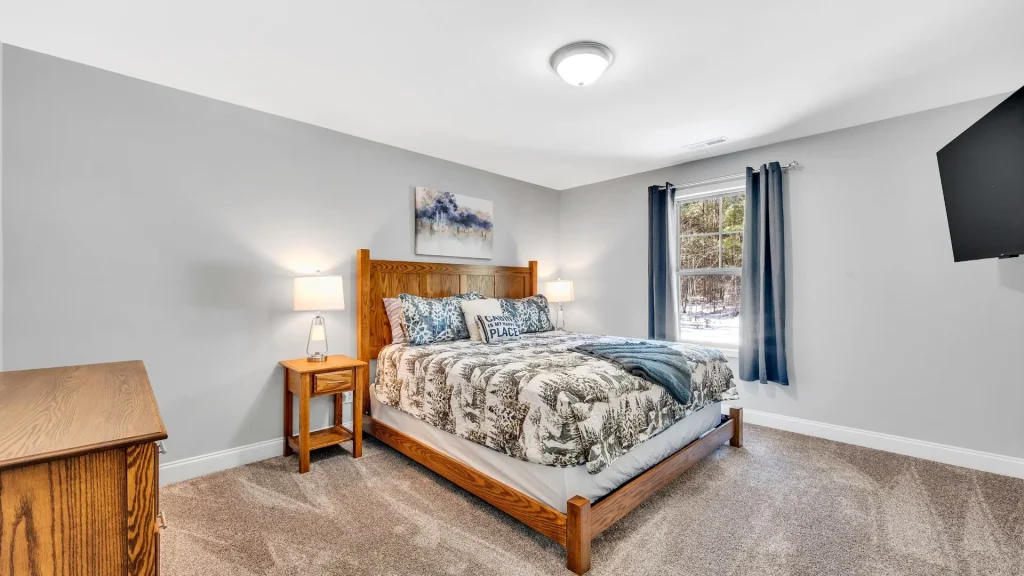 Bedroom with a wooden bed, two nightstands, and lamps; window with blue curtains to the right.