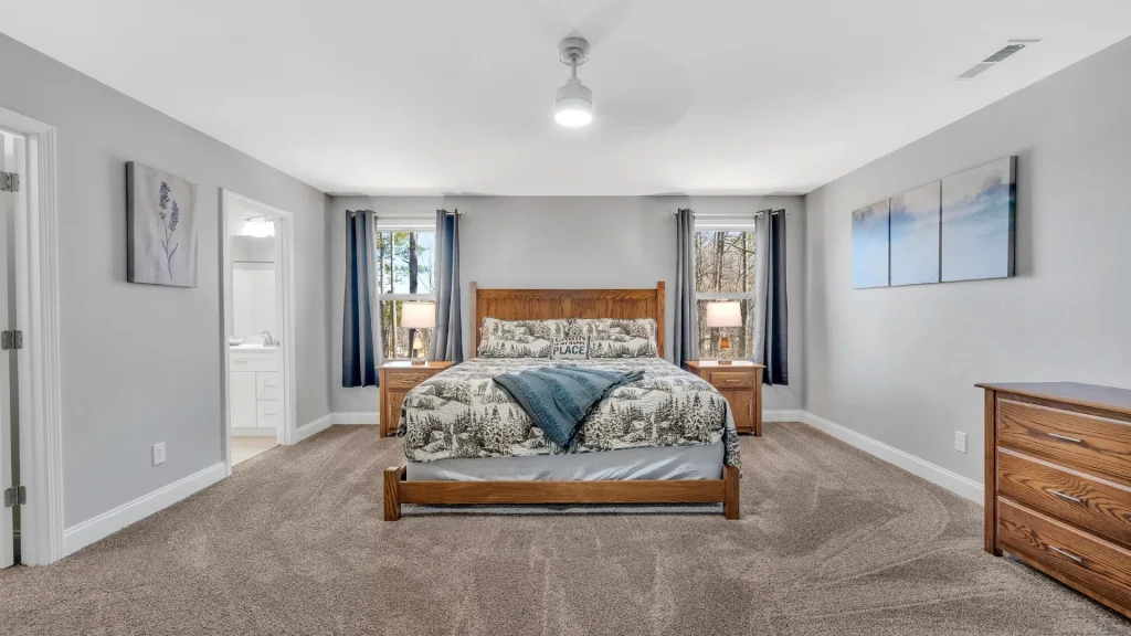 Bedroom with a wooden bed, two nightstands, and gray walls; twin windows with dark curtains flank the bed and a landscape painting on the wall.