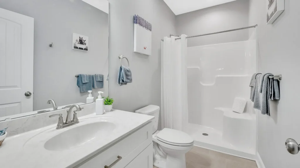 Bright modern bathroom with a white vanity, gray walls, and a bathtub with a white curtain in the background.