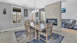 whipering-winds-slider-images 26 | Swack Vacations Open-plan dining area with a wooden table and six chairs, hanging glass pendant lights, and a stone fireplace divider separating living room.