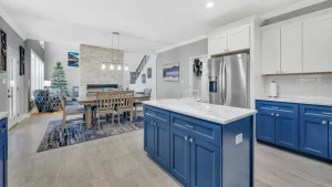 whipering-winds-slider-images 33 | Swack Vacations Open-concept kitchen and dining area featuring a blue island, stainless steel fridge, and marble countertops, with a living room and fireplace in the background.