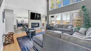 Open living room with gray sectional, two patterned chairs, coffee tables, a stone fireplace, and a wall-mounted TV above.