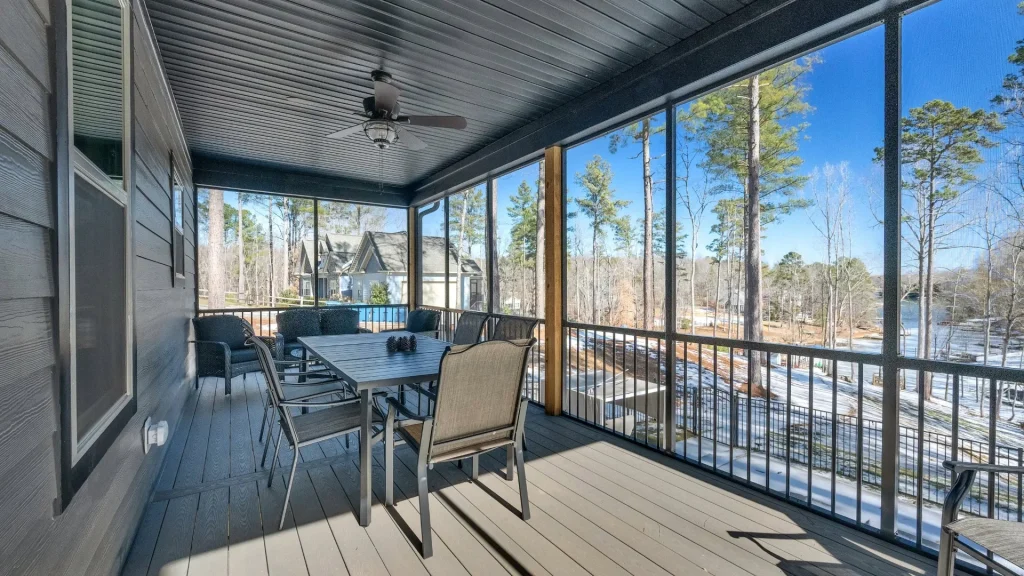 Screened-in porch with a rectangular dining table and multiple chairs, overlooking a snowy yard with tall trees and neighboring houses.