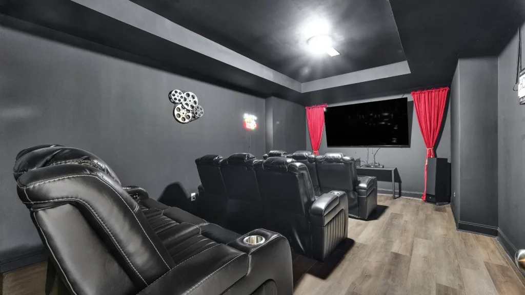 Home theater room with multiple black leather recliners facing a large wall-mounted TV and red curtains on either side.