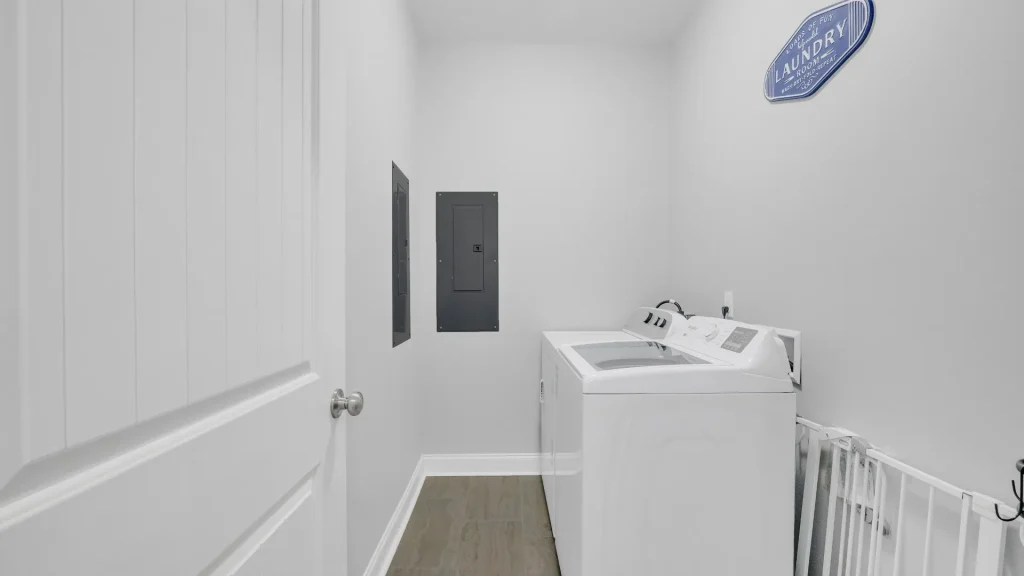 Laundry room with a white top-loading washing machine against the right wall, plus utility panels on the wall and a blue laundry sign above.